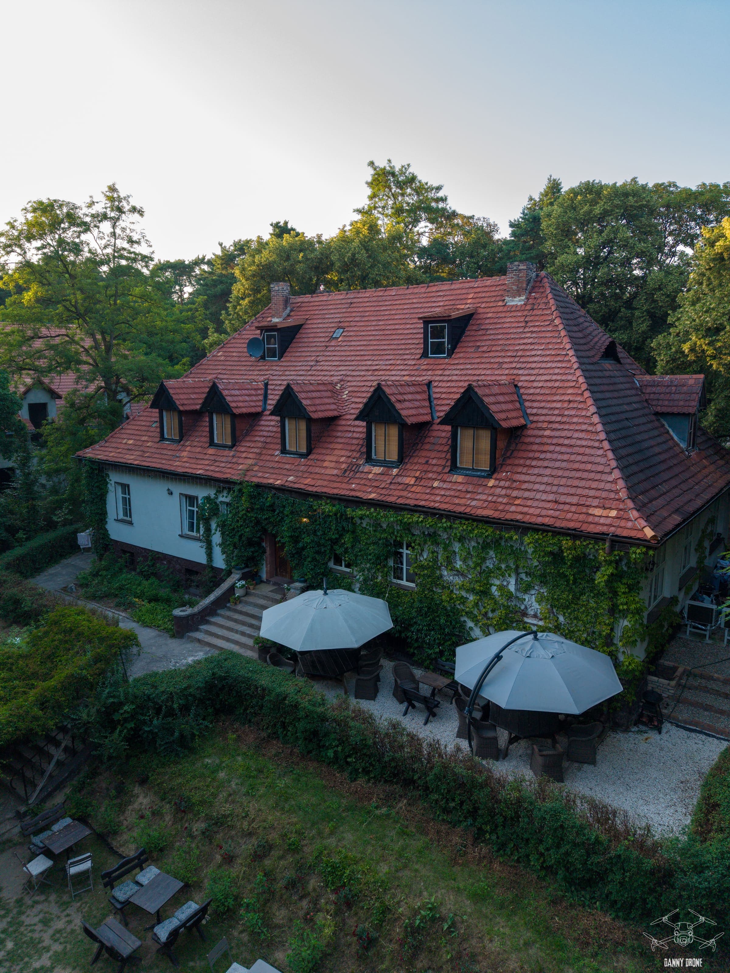 Pensjonat z drona - elewacja porośnięta zielenią i taras z parasolami